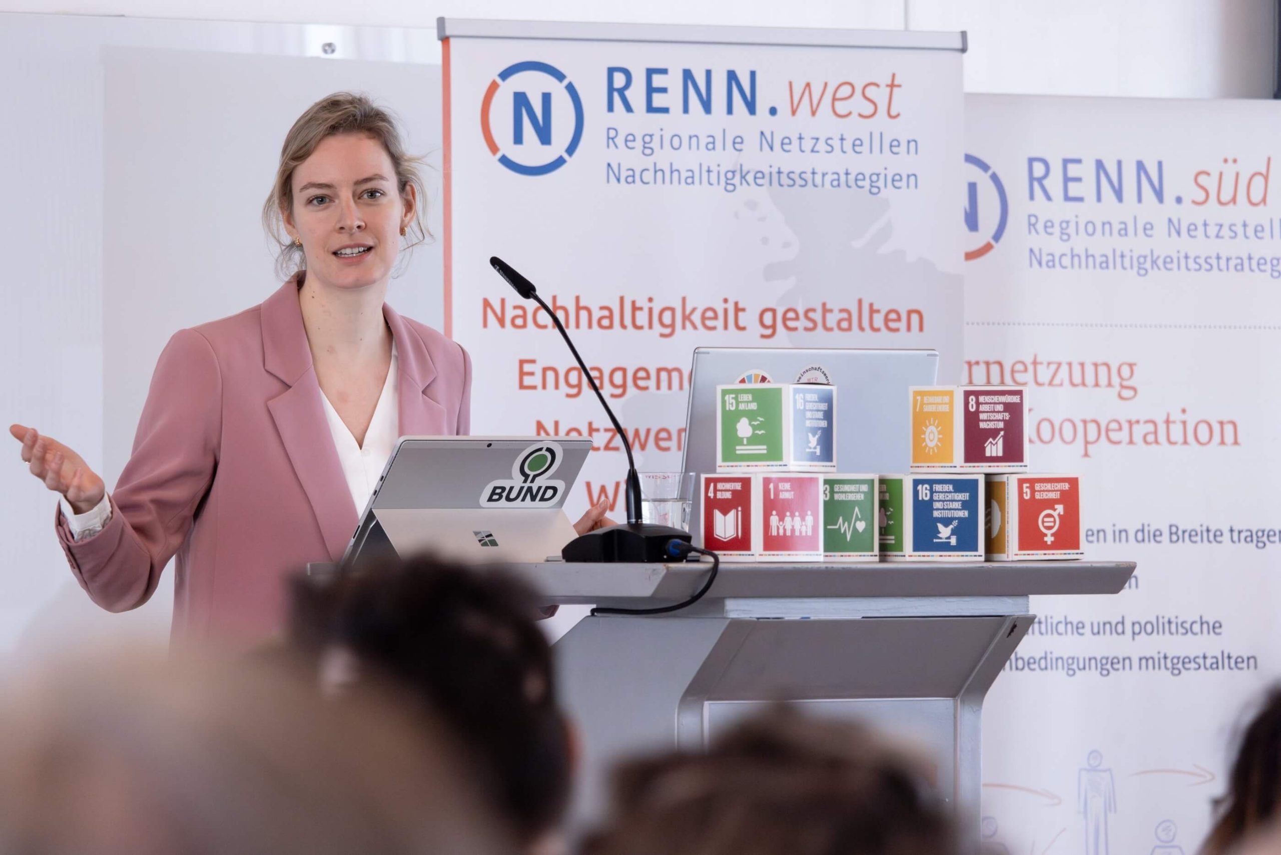 Myriam Rapior, stellvertretende Bundesvorsitzende des BUND e.V. und RNE-Mitglied hält einen Vortrag auf den RENN Tagen 2023. Neben ihr sind Banner der RENN sowie SDG Würfel zu sehen.