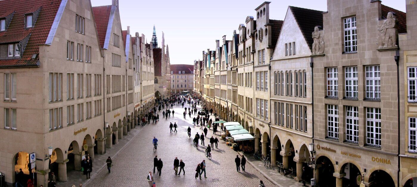Auf dem Foto sieht man die Altstadt von Müster mit einigen Marktständen und Fußgängern.