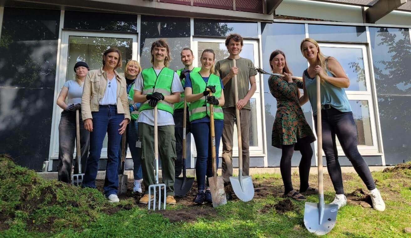 Auf dem Foto sieht man neun Personen, die mit Harken und Spaten vor einem Gebäude stehen. Beim Auftakt der Deutschen Aktionstage Nachhaltigkeit pflanzten Freiwillige Blumenwiesen, Seedbombs und hängten Vogelhäuser auf dem Campus der Universität Hamburg auf. Foto: Myriam Rapior