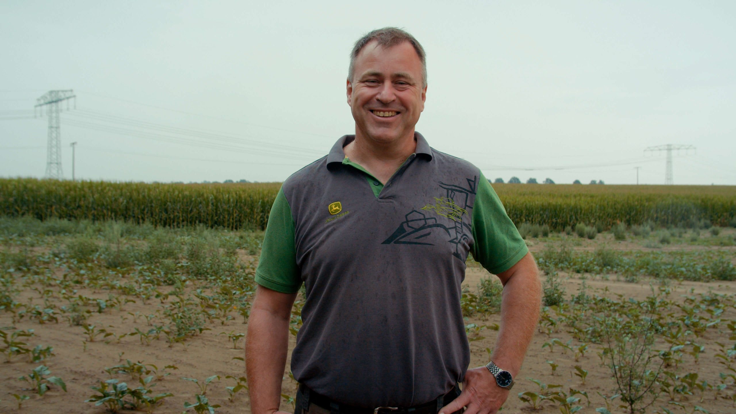 Marco Gemballe steht auf einem Feld. Im Hintergrund sieht man mehrere Strommaste. Marco Gemballa ist Geschäftsführer der Agrargesellschaft Zinzow in Mecklenburg-Vorpommern. Foto: Die Grüne Filmagentur © RNE|