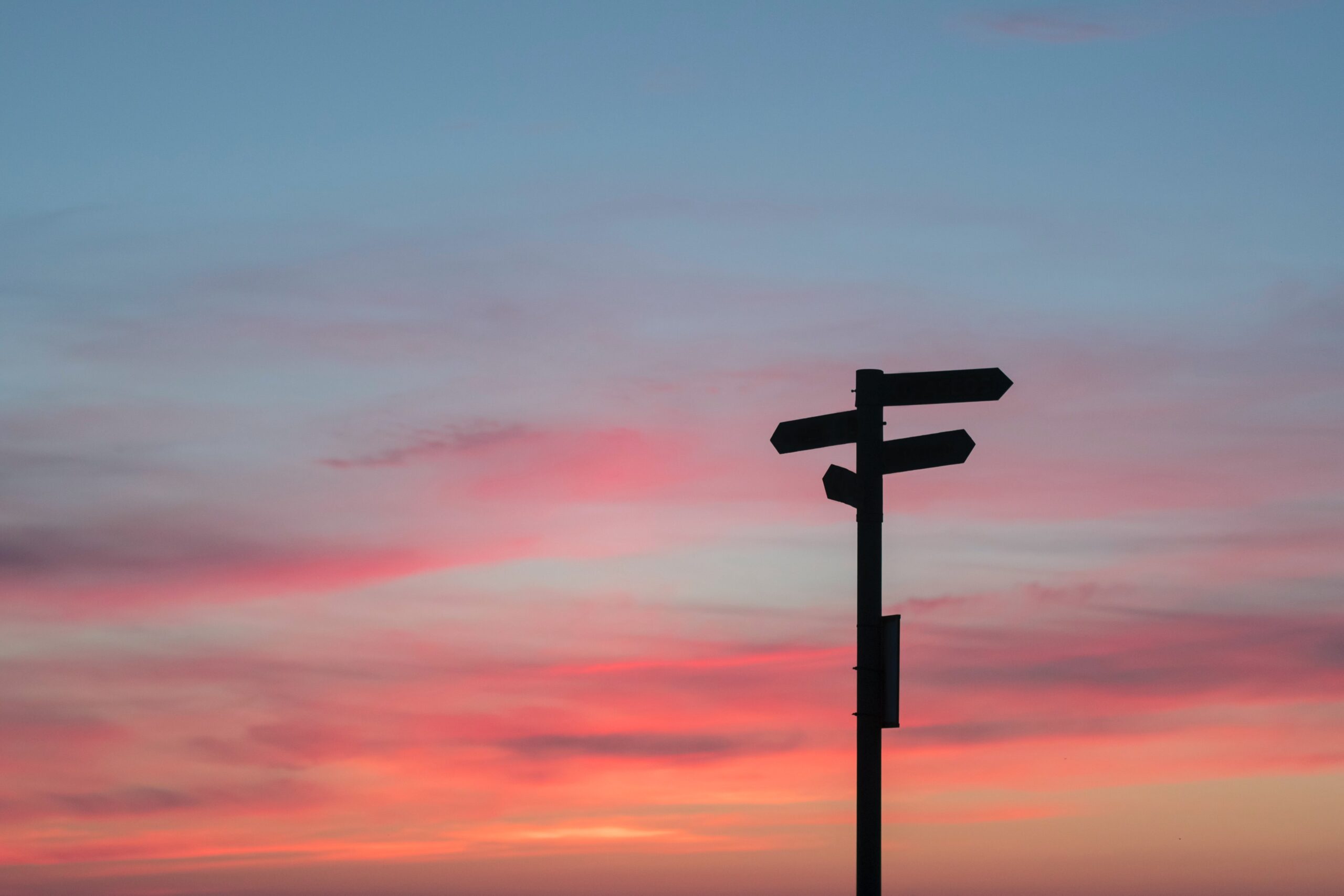 Ein Wegweiserschild vor Wolken und Himmel nach Sonnenuntergang © Foto: Javier Allegue Barros, unsplash